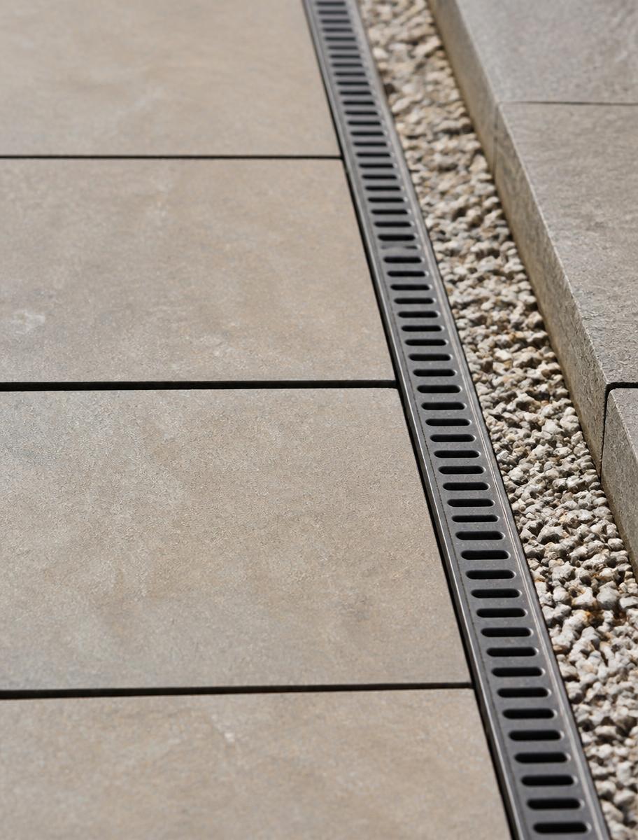 Detail eines Plattenbelags mit Entwässerungsrinne und Kiesstreifen