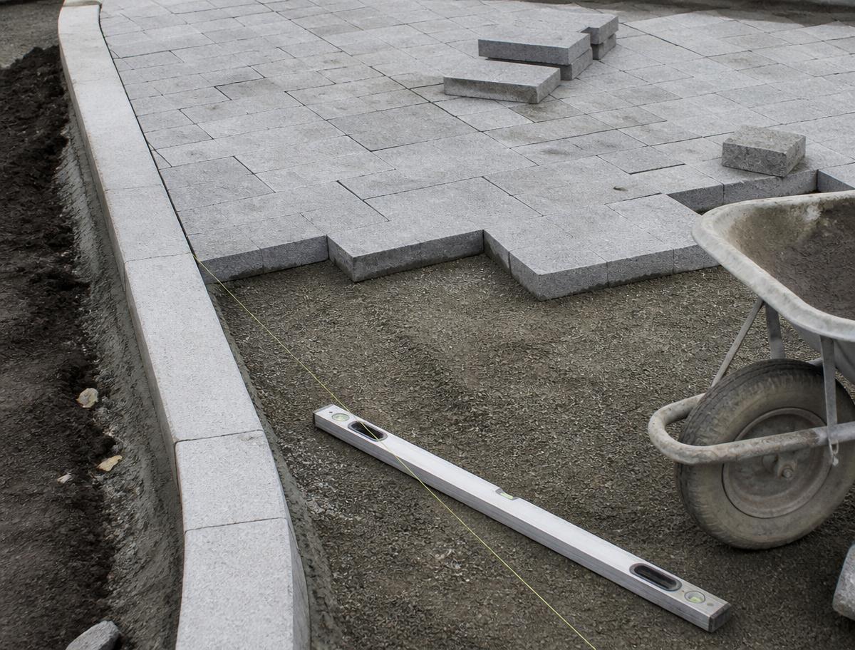 Pflasterfläche im Bau mit Schnurgerüst, Wasserwaage und verdichtetem Unterbau